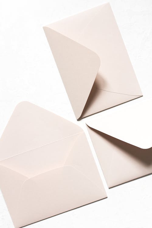 Overhead view of simple light beige unsealed envelops with triangular seal flap in light of lamps on white background