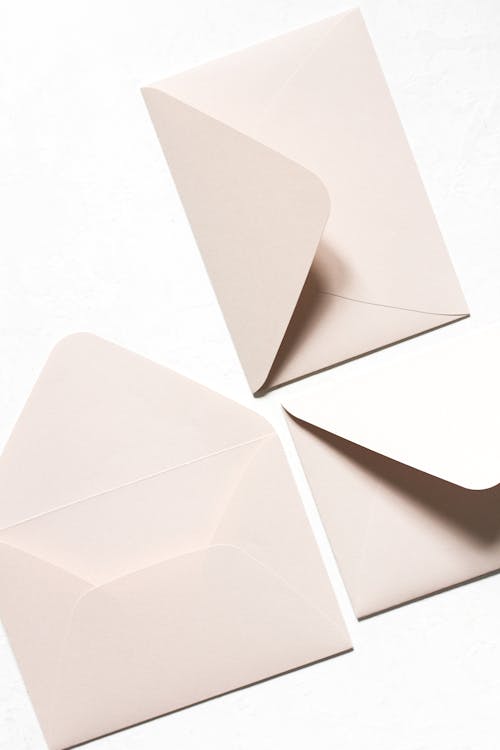 Free Overhead view of simple light beige unsealed envelops with triangular seal flap in light of lamps on white background Stock Photo