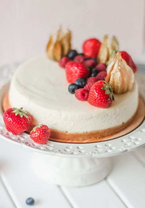Free White round delicious cake decorated with blackberries and strawberries on white table in bright kitchen Stock Photo