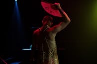 在灯光昏暗的夜总会里，一名表演者手持扇子，展示着夜生活和行为艺术