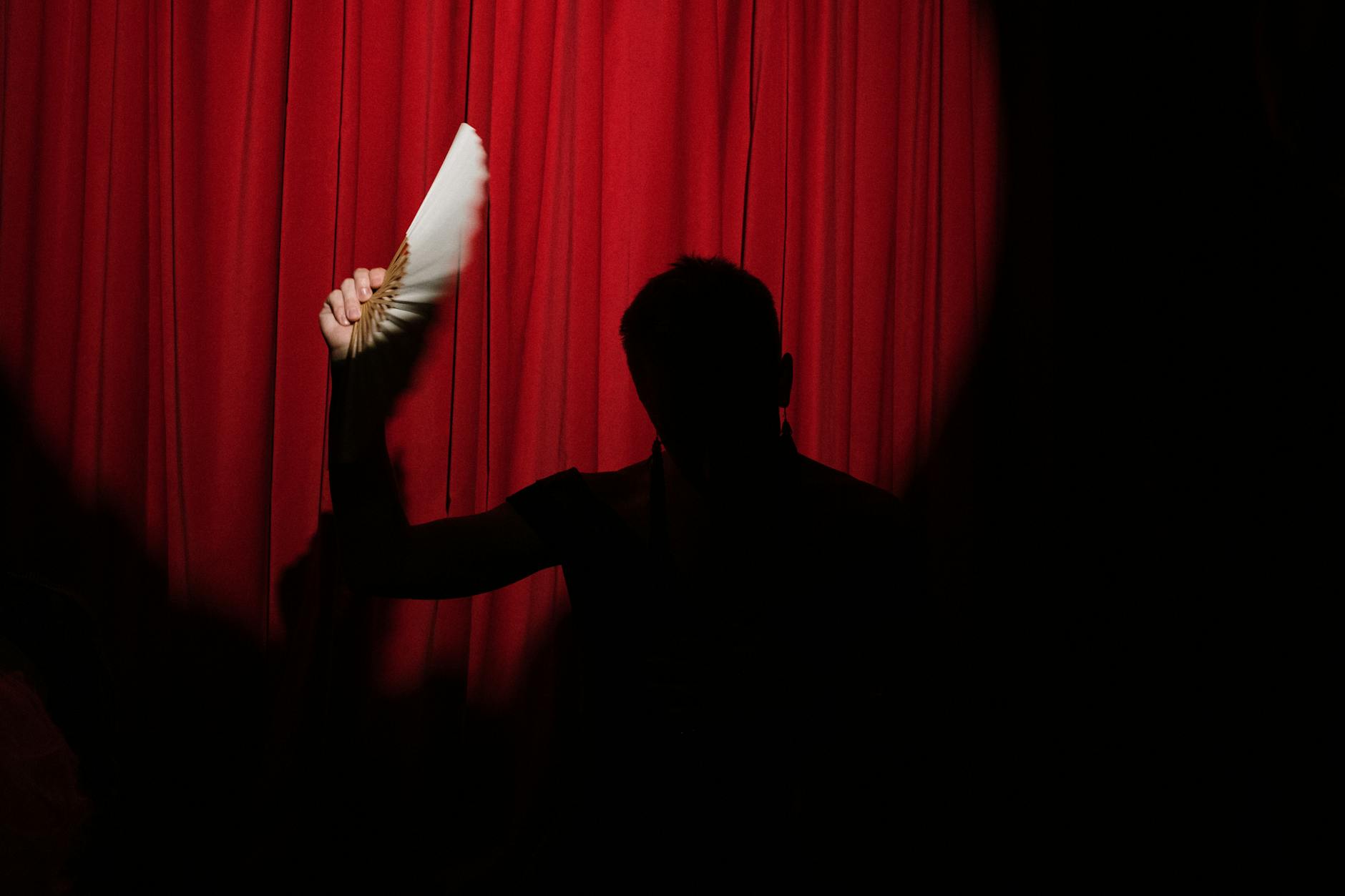 Silhouette of a Person Holding a Hand Fan on Stage
