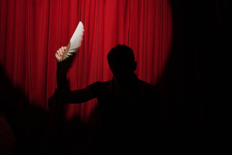 Silhouette Of A Person Holding A Hand Fan On Stage