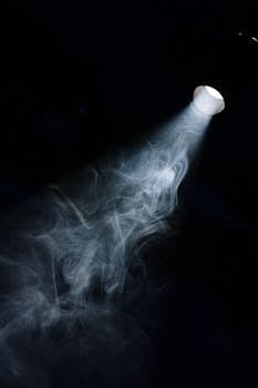 A beam of light penetrates through smoke in a dark setting, creating a moody atmosphere.