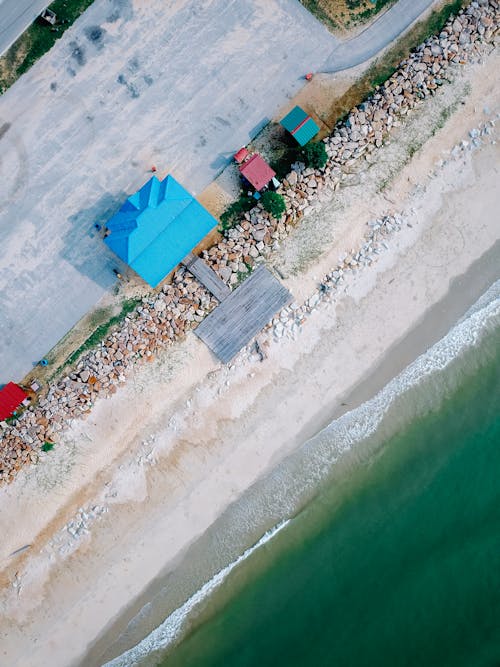 Drone view of small houses located near sandy beach of wavy ocean on sunny day