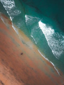 Picturesque aerial view of wide sandy beach washed by foamy waves of powerful turquoise ocean