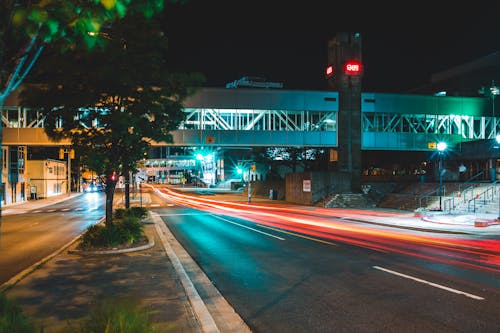 Long exposure urban asphalt road with pedestrian overpass located in modern city at night