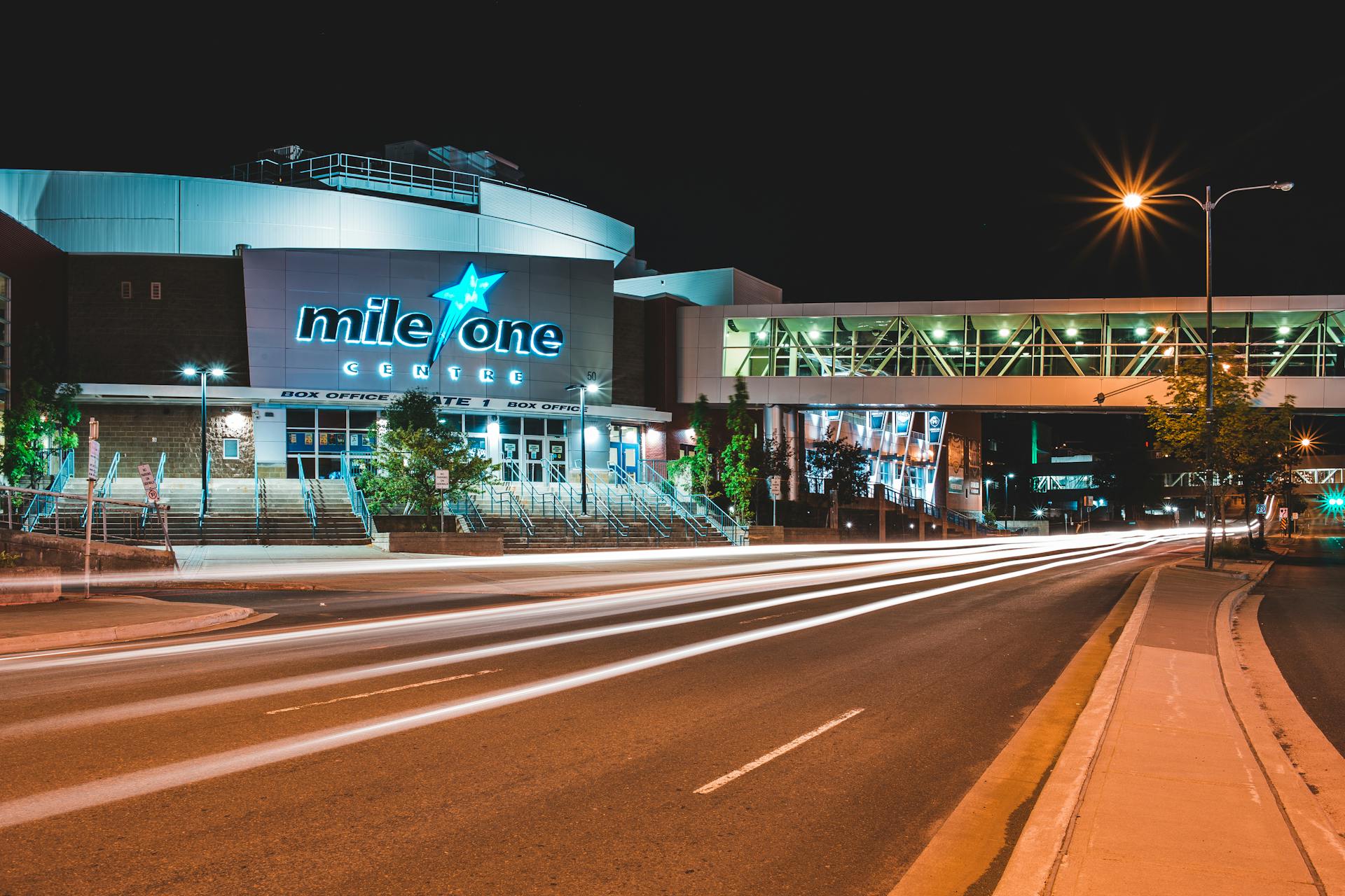 Illuminated Mile One Centre with dynamic vehicle light trails at night, showcasing urban architecture.