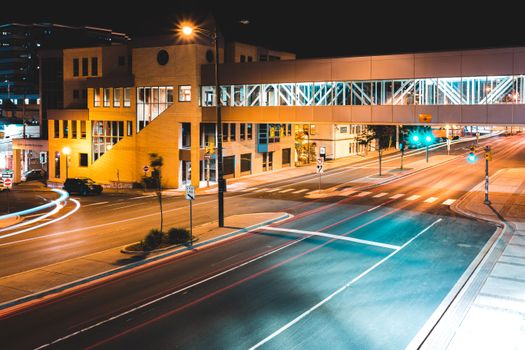 A vibrant night view of an urban crossroad with an illuminated pedestrian bridge, showcasing contemporary architecture.