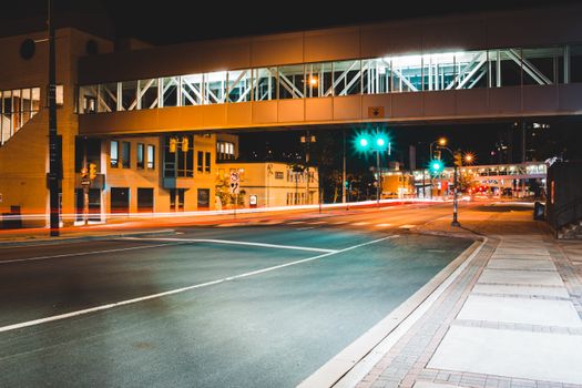 Illuminated asphalt road with traffic lights and modern building with above ground pedestrian crossing