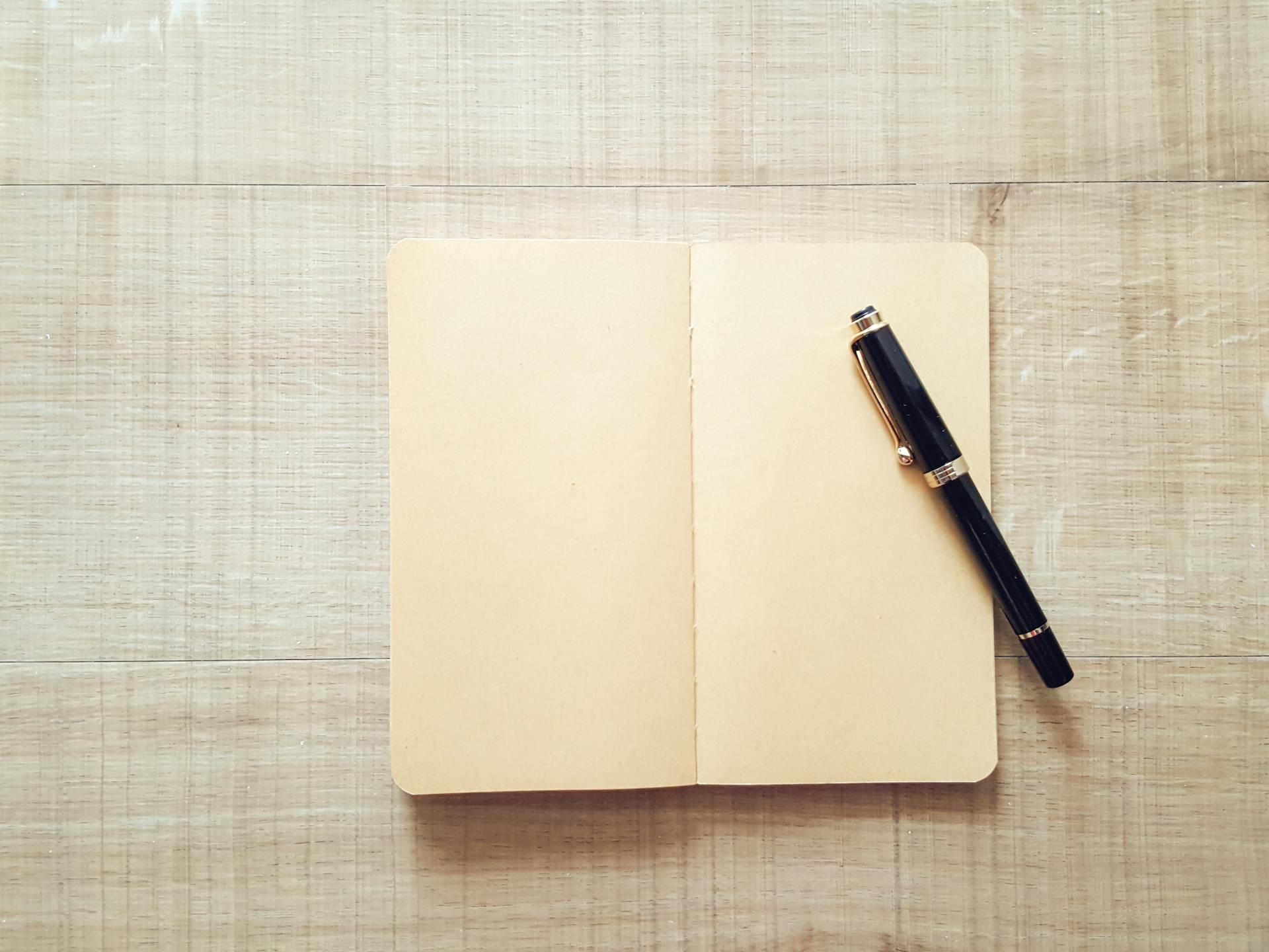 Minimalist top-view image of an open notebook with a pen on a wooden surface for writing inspiration.