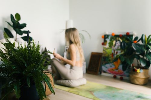 Free A woman practices meditation indoors surrounded by plants, promoting wellness and relaxation. Stock Photo