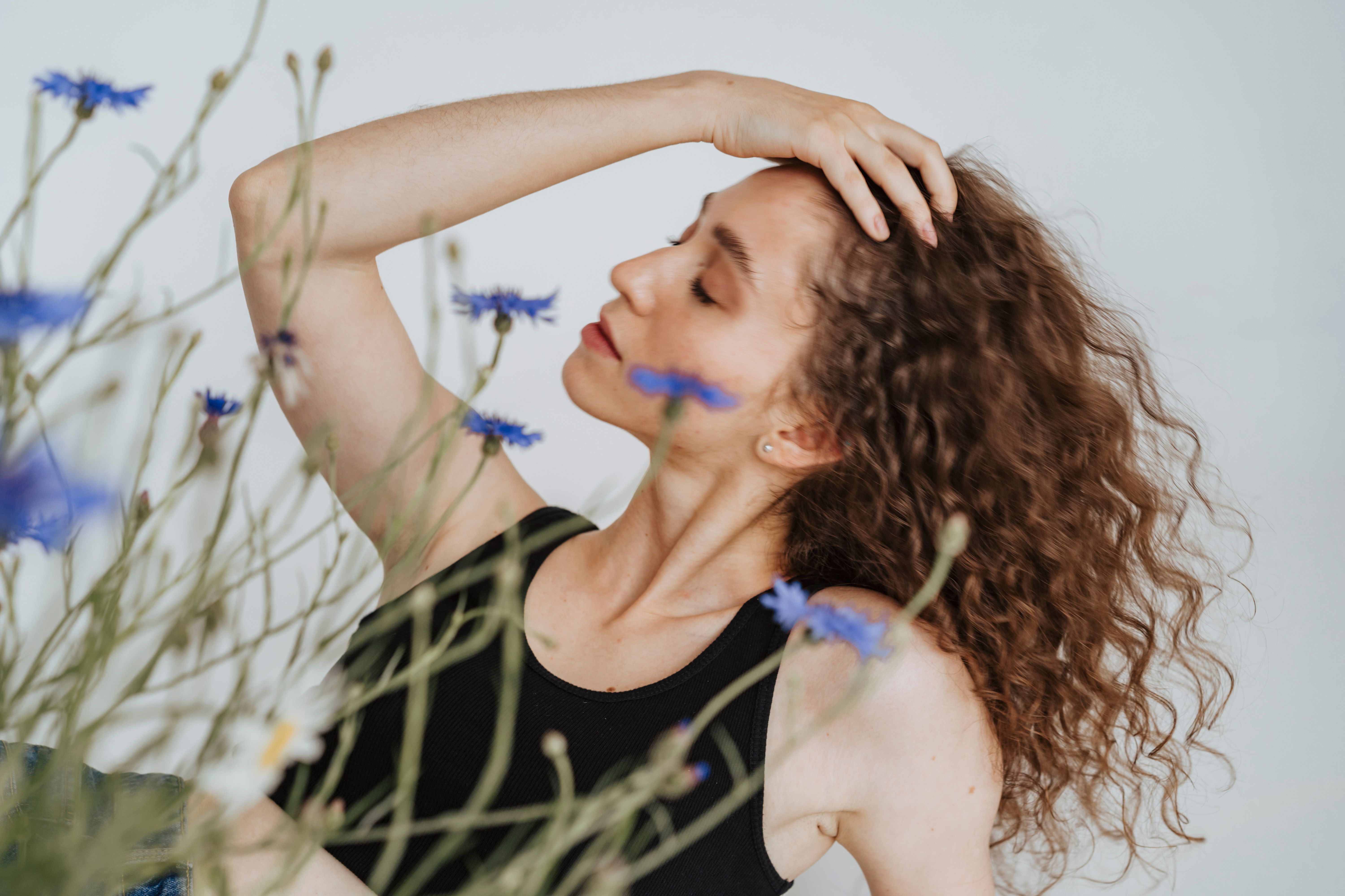 A serene portrait of a young woman with curly hair and wildflowers in focus, showcasing natural beauty.
