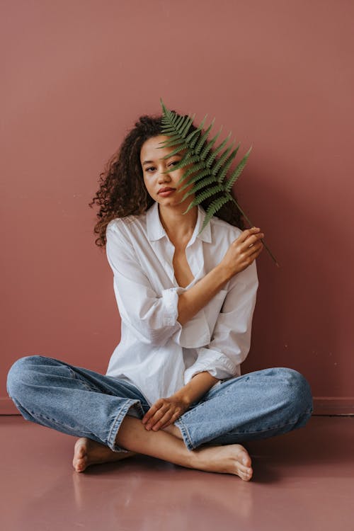 Woman Sitting on the Floor While Holding a Fern Leaf