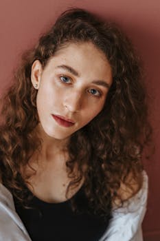 在粉红色的背景下，一位卷发、蓝眼睛的女性肖像显得格外优雅