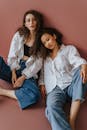 两名留着卷发、身穿牛仔布和白衬衫的女性，在朴素的背景下摆出时尚的姿势