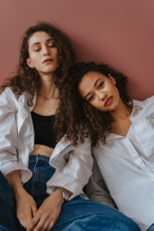 Free Portrait of two women in casual fashion, set against a warm-toned backdrop. Stock Photo