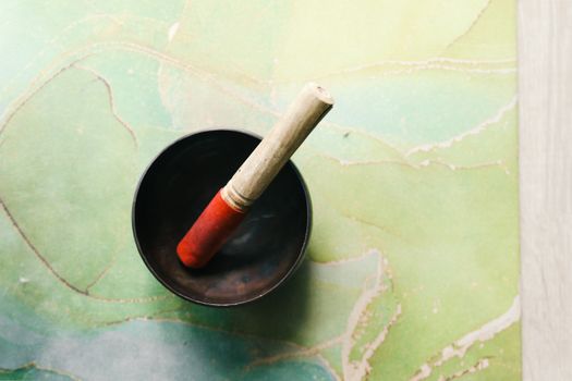 Above view of a Tibetan singing bowl with wooden mallet on a green mat for meditation.