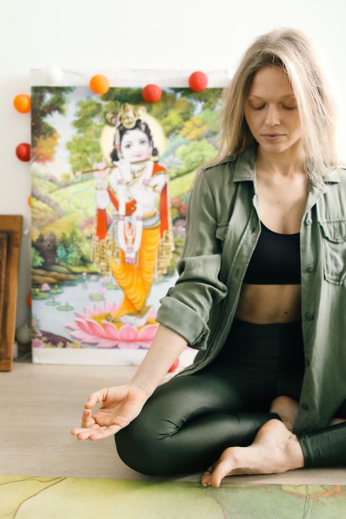 Free A serene scene of a young woman meditating indoors in front of vibrant Hindu artwork. Stock Photo