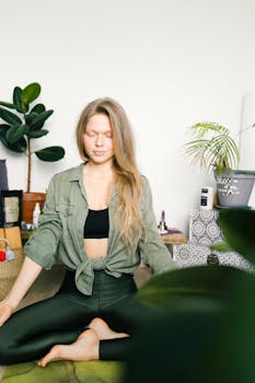 A woman in lotus pose meditates in a serene indoor setting, promoting wellness and relaxation.
