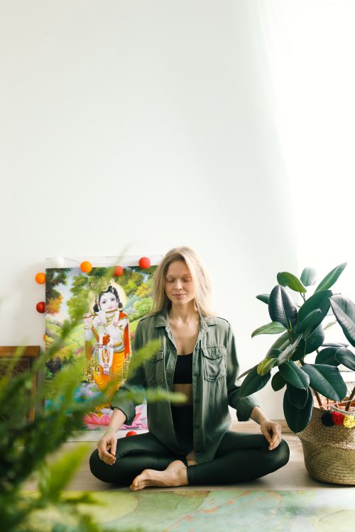 Free Woman meditating indoors in a yoga pose, surrounded by plants, embracing peace and wellness. Stock Photo