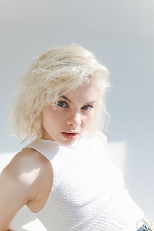Free Elegant studio portrait of a young blonde woman in a white top, illuminated by natural light. Stock Photo