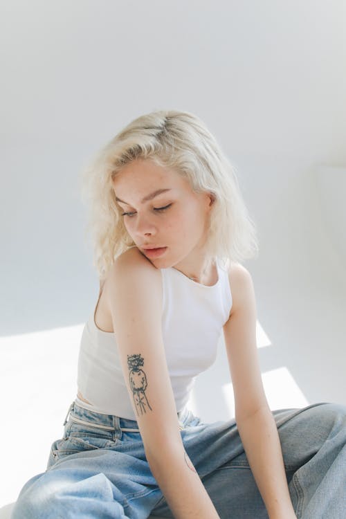 Young Woman in a White Top and Jeans Sitting in a Bright Room 