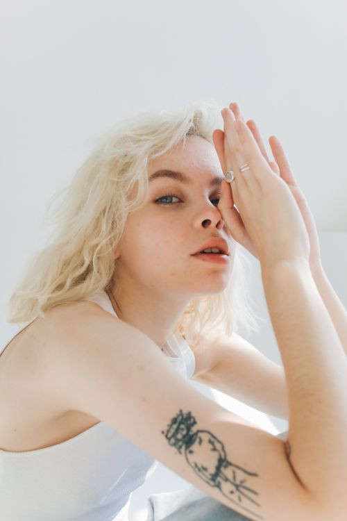 Free Close-up portrait of a blonde woman with a tattoo, showcasing a serene expression in a bright setting. Stock Photo