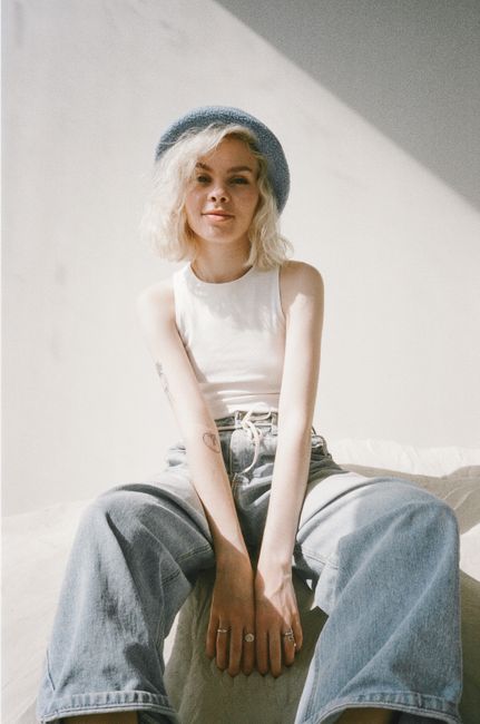 A cheerful blonde woman in casual fashion sits joyfully indoors with a bright hue.
