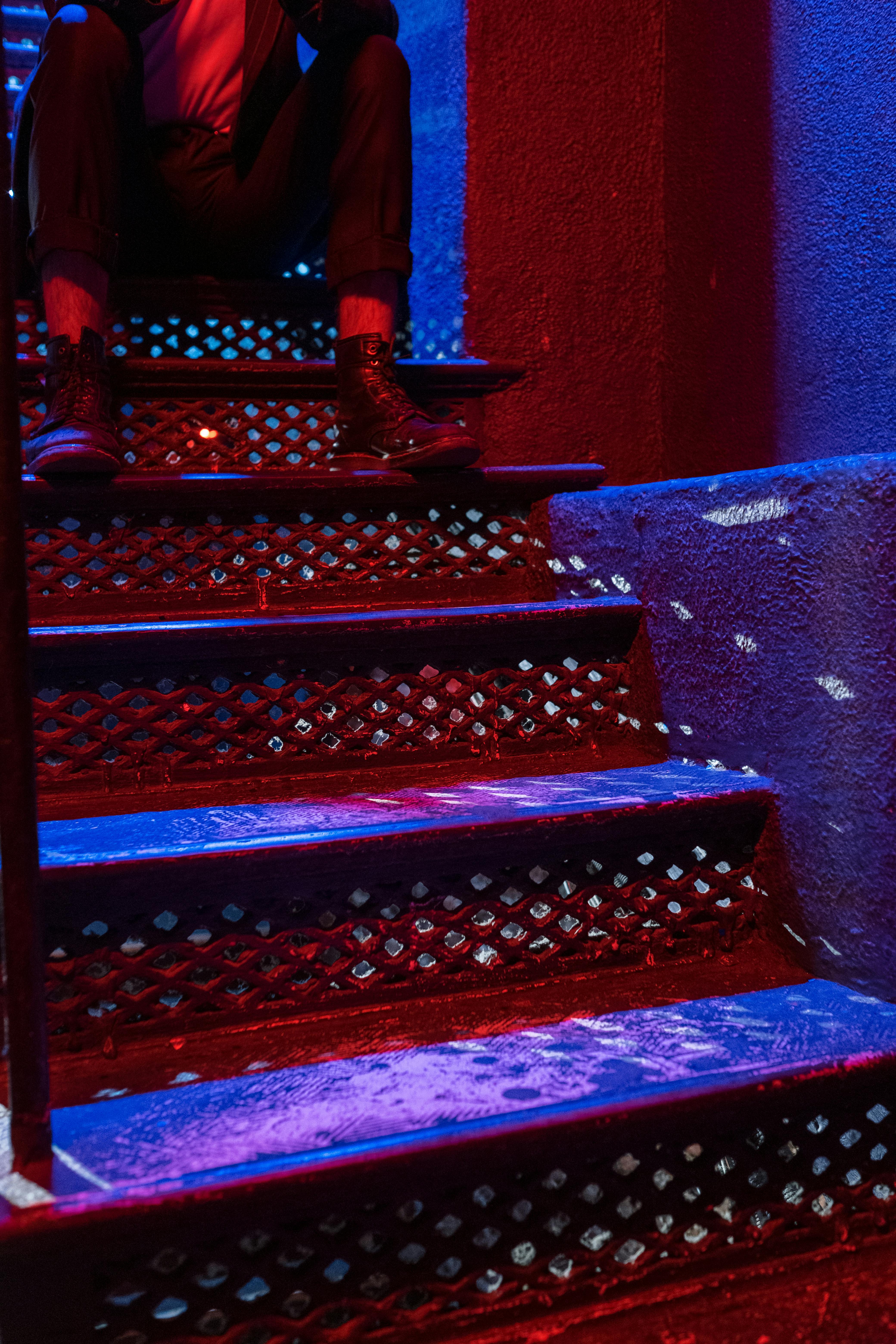 Free A stylish man sitting on nightclub stairs with vibrant lighting. Stock Photo