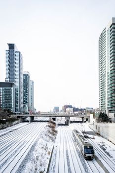 A train travels through snowy railway tracks with Toronto skyscrapers in view.