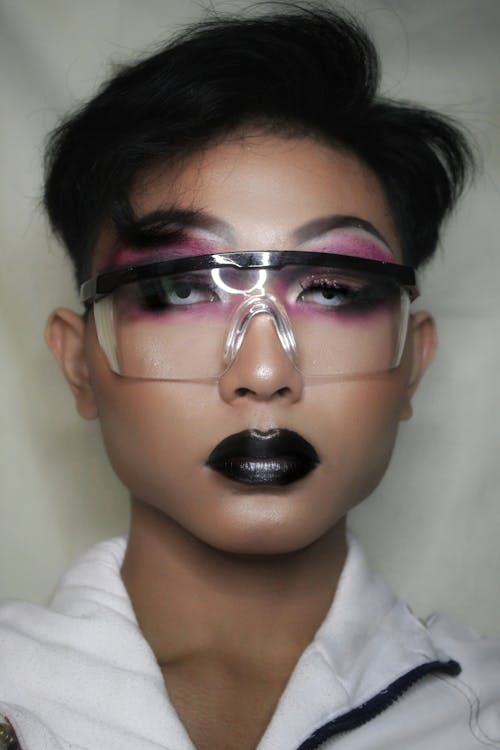 Young creative makeup artist with shiny colorful makeup and protective glasses looking at camera