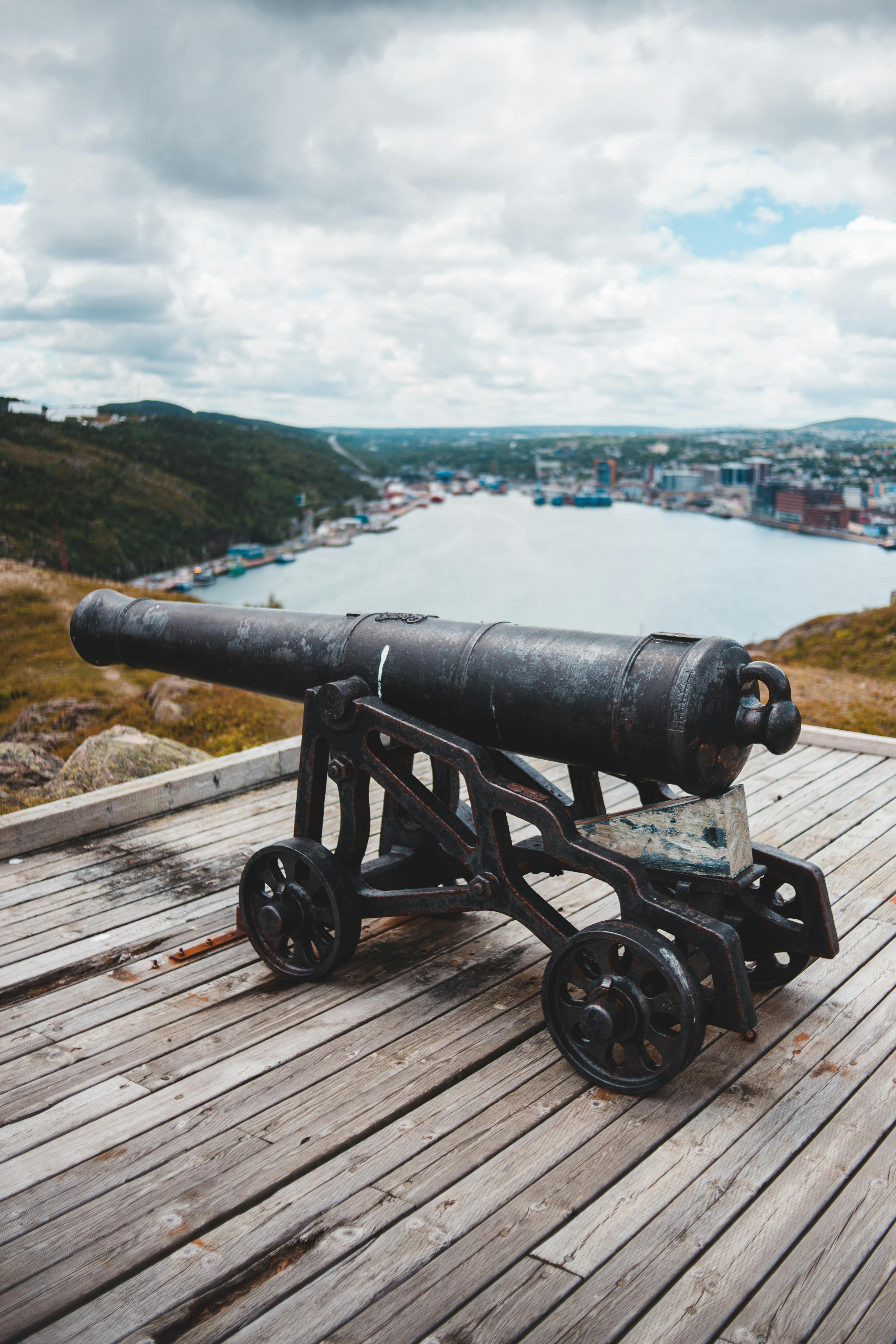 Antique black metal cannon placed on wooden terrace against landscape with hills and lake and town