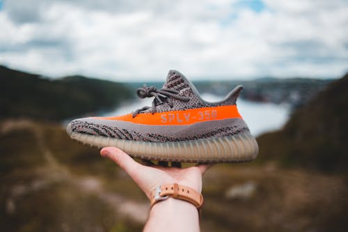 Free Crop unrecognizable person holding gray sneaker with vivid orange line in hand against picturesque scenery of nature Stock Photo