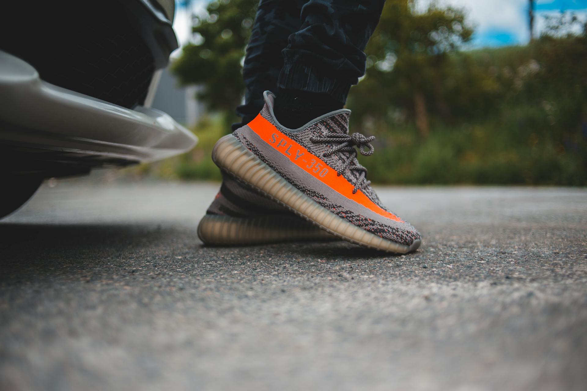 Anonymous person in grey textile sneakers with orange line standing on asphalt road near car