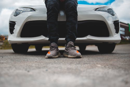 Person in Black Pants and Gray Sneakers Standing Beside White Car