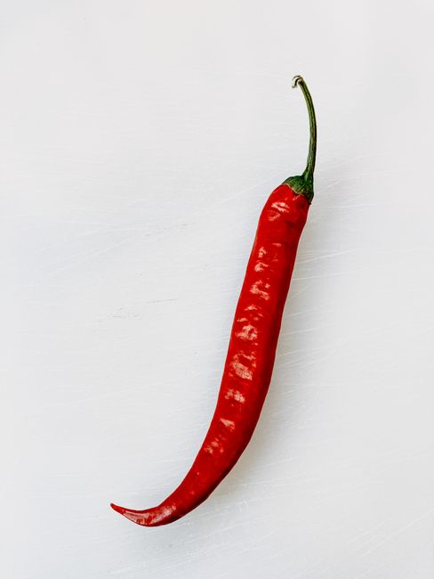 Close-up of a vibrant red chili pepper on a stark white background, ideal for spice themes.