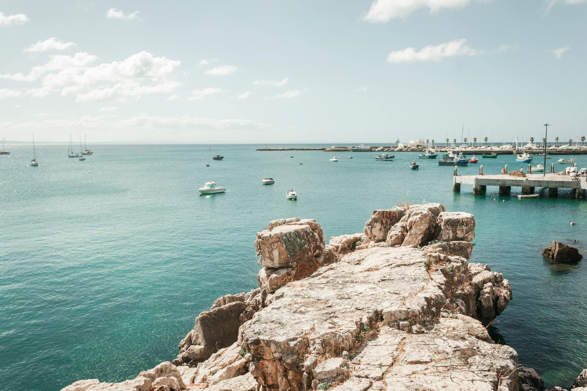 Beautiful coastal scene in Cascais, Lisbon with boats and rocky shoreline.