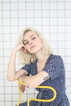 一位身穿蓝色圆点连衣裙的金发女子，若有所思地坐在瓷砖背景前