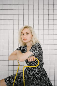 一名年轻的金发女子坐在网格背景前的黄色椅子上