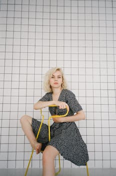 一位年轻女子自信地坐在黄色椅子上，背后是瓷砖墙，散发着现代而沉思的氛围