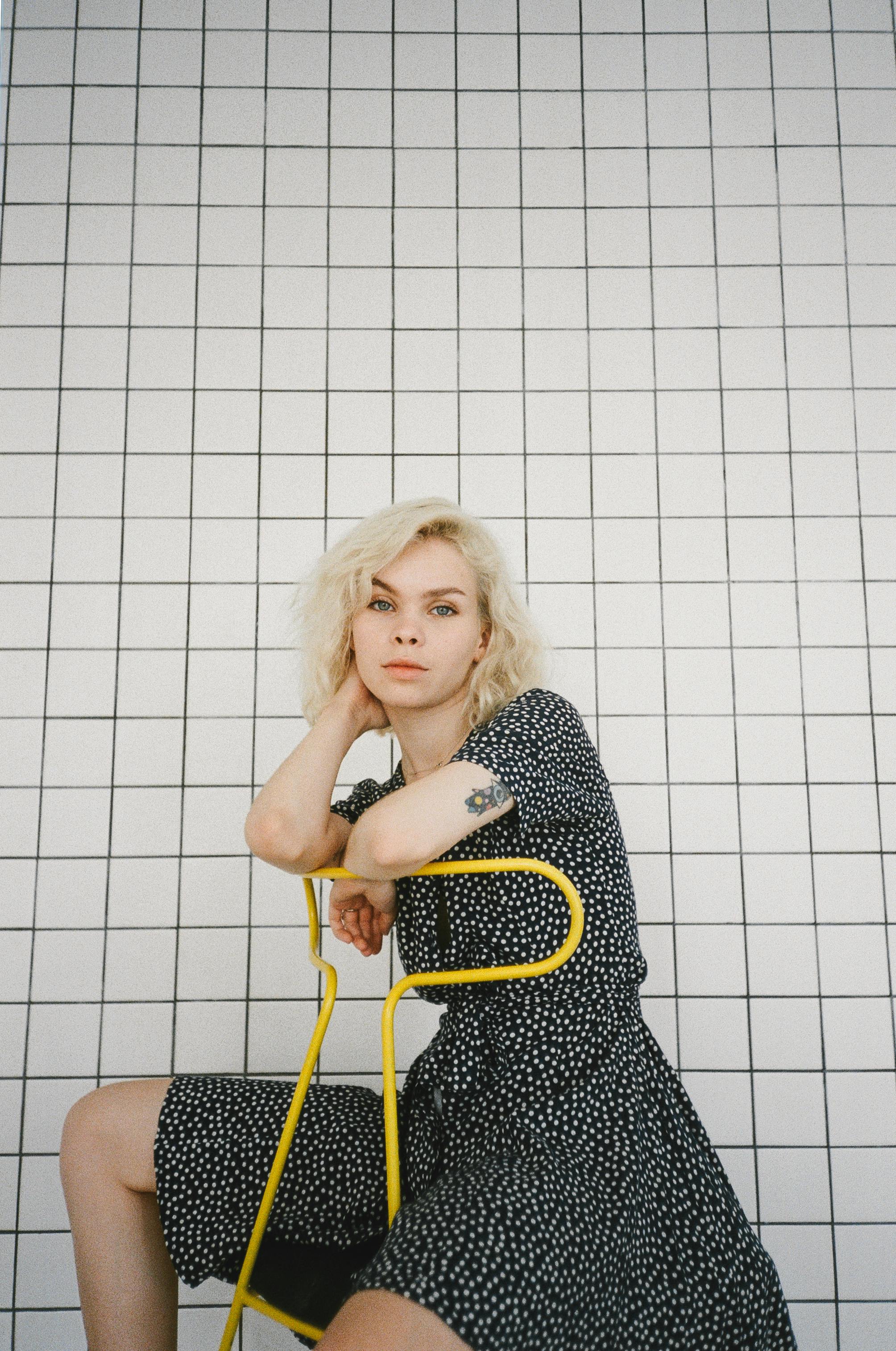 穿着圆点连衣裙的金发少女坐在网格背景的椅子上