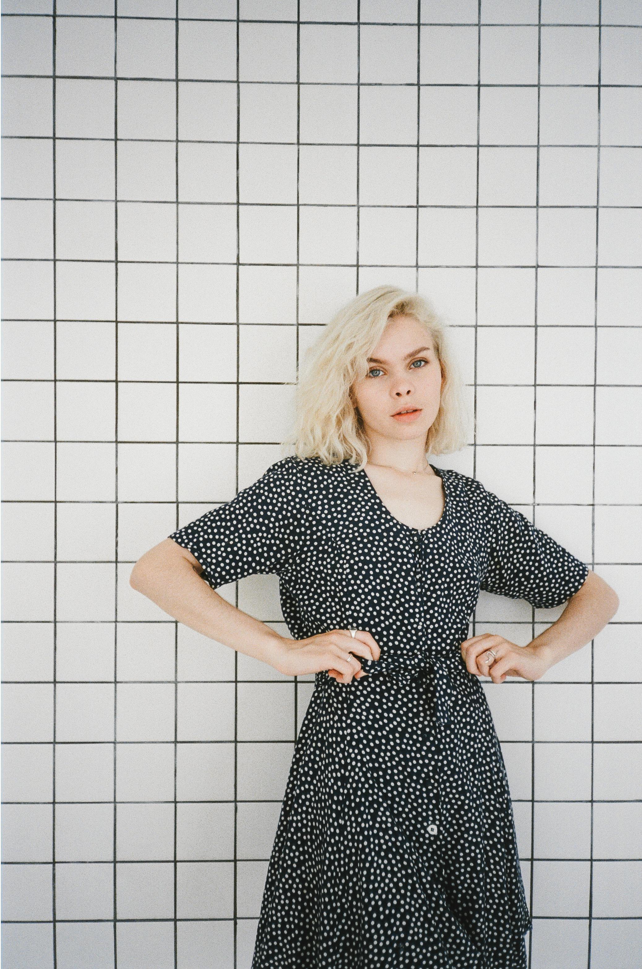 girl in black and white polka dot dress standing beside white wall