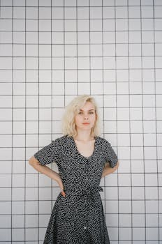 Young woman with blond hair posing confidently in a polka dot dress against a grid-patterned wall.