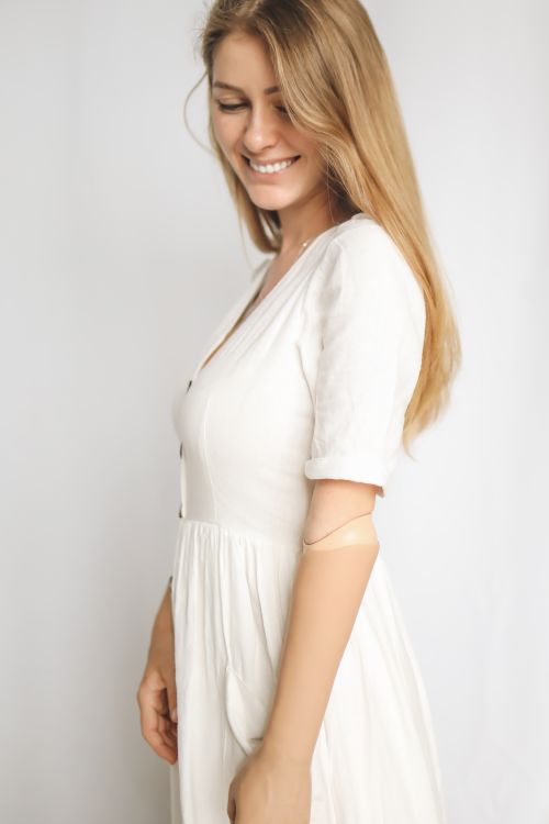 Free A young caucasian woman in a white dress smiles while displaying a prosthetic arm, with an elegant pose. Stock Photo