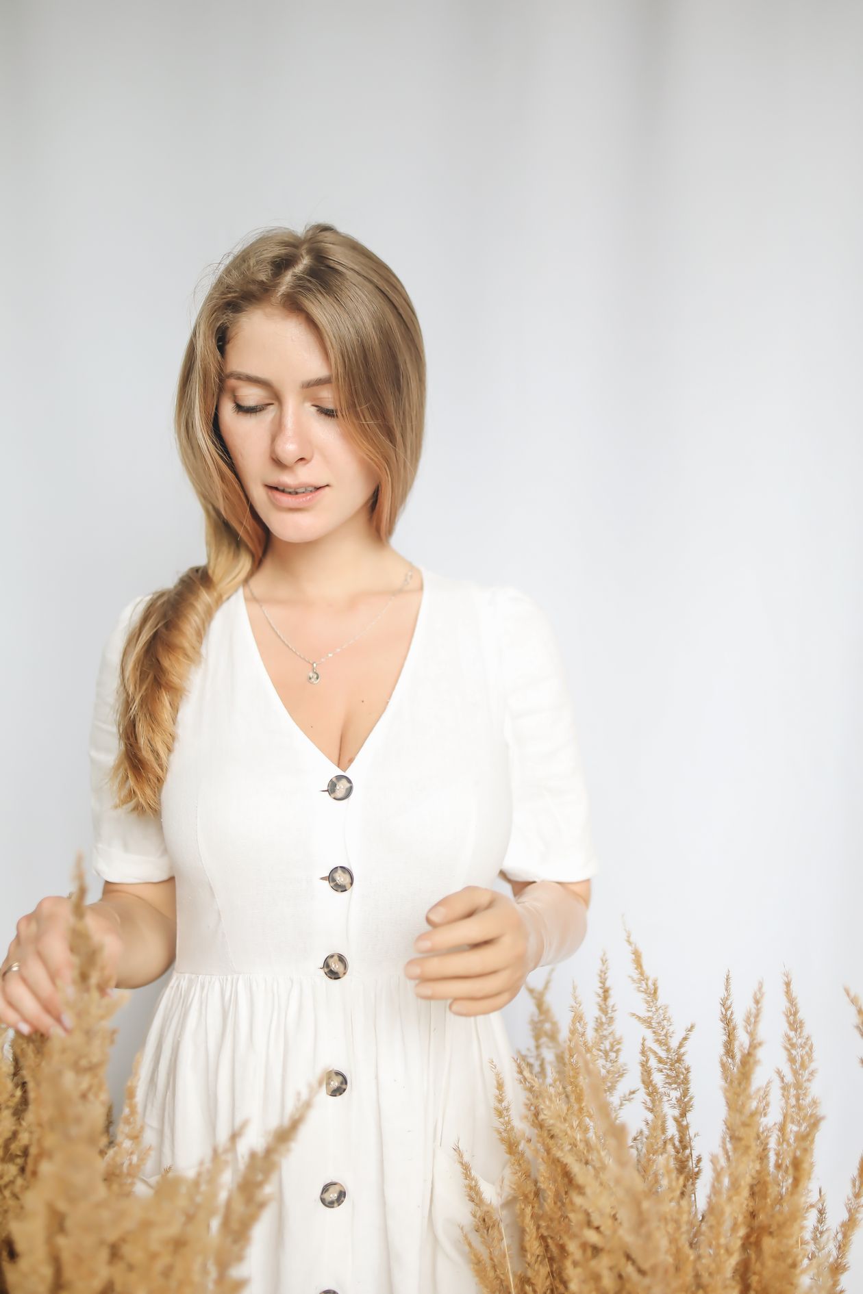 Woman in a white button-front short dress with dried wheat stalks
