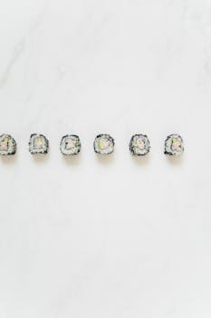 Minimalist arrangement of sushi rolls with salmon and avocado on a light marble background.