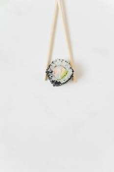 A single sushi roll with chopsticks on a clean white surface, showcasing modern food presentation.