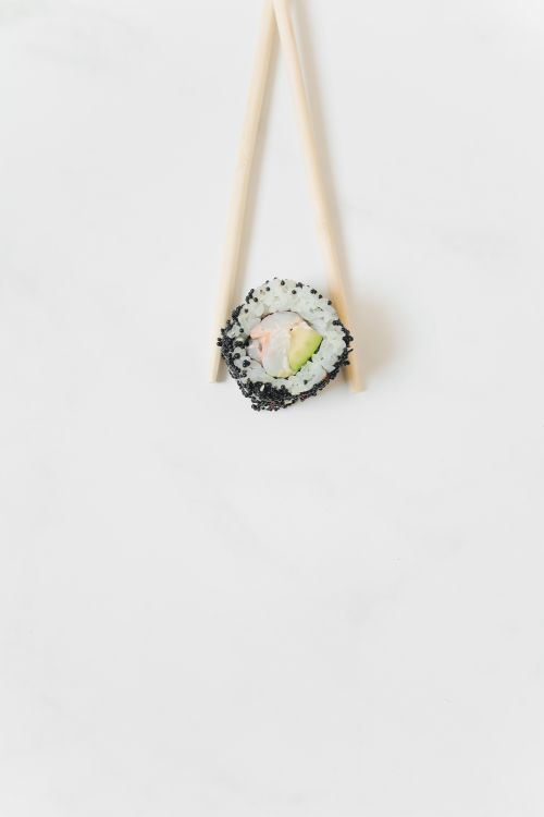 Free A single sushi roll with chopsticks on a clean white surface, showcasing modern food presentation. Stock Photo