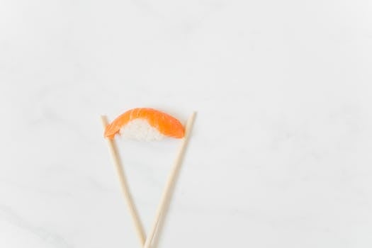Close-up of nigiri sushi with chopsticks on a marble surface, showcasing minimalist Japanese cuisine.