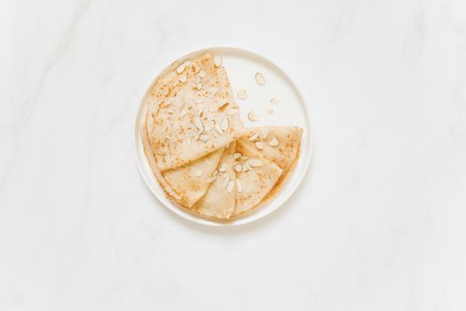 Tasty homemade crepes topped with sliced almonds on a white plate, perfect for a sweet treat.